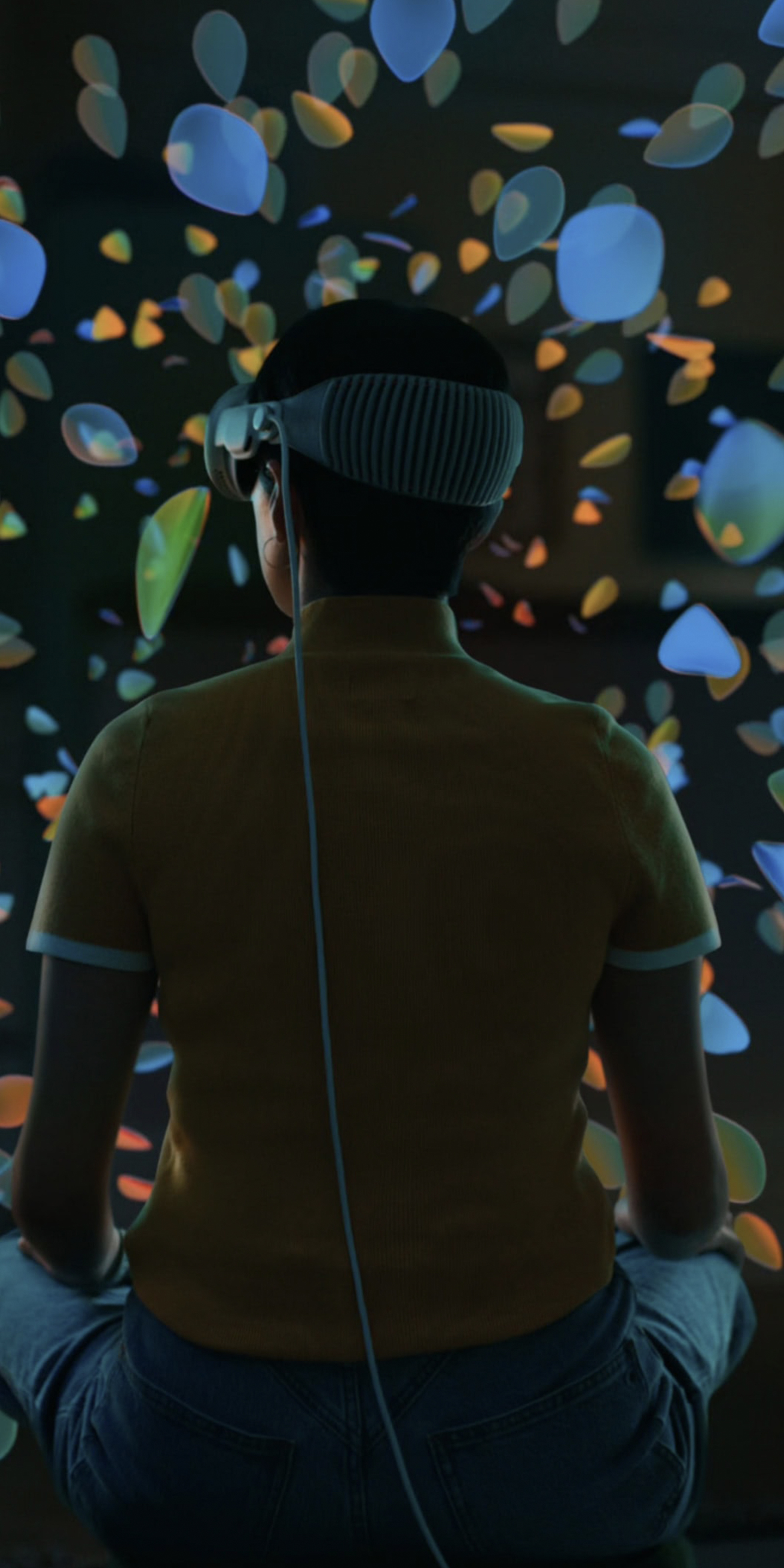 A person wearing an Apple Vision Pro headset viewing a mixed reality scene of colourful glass petals