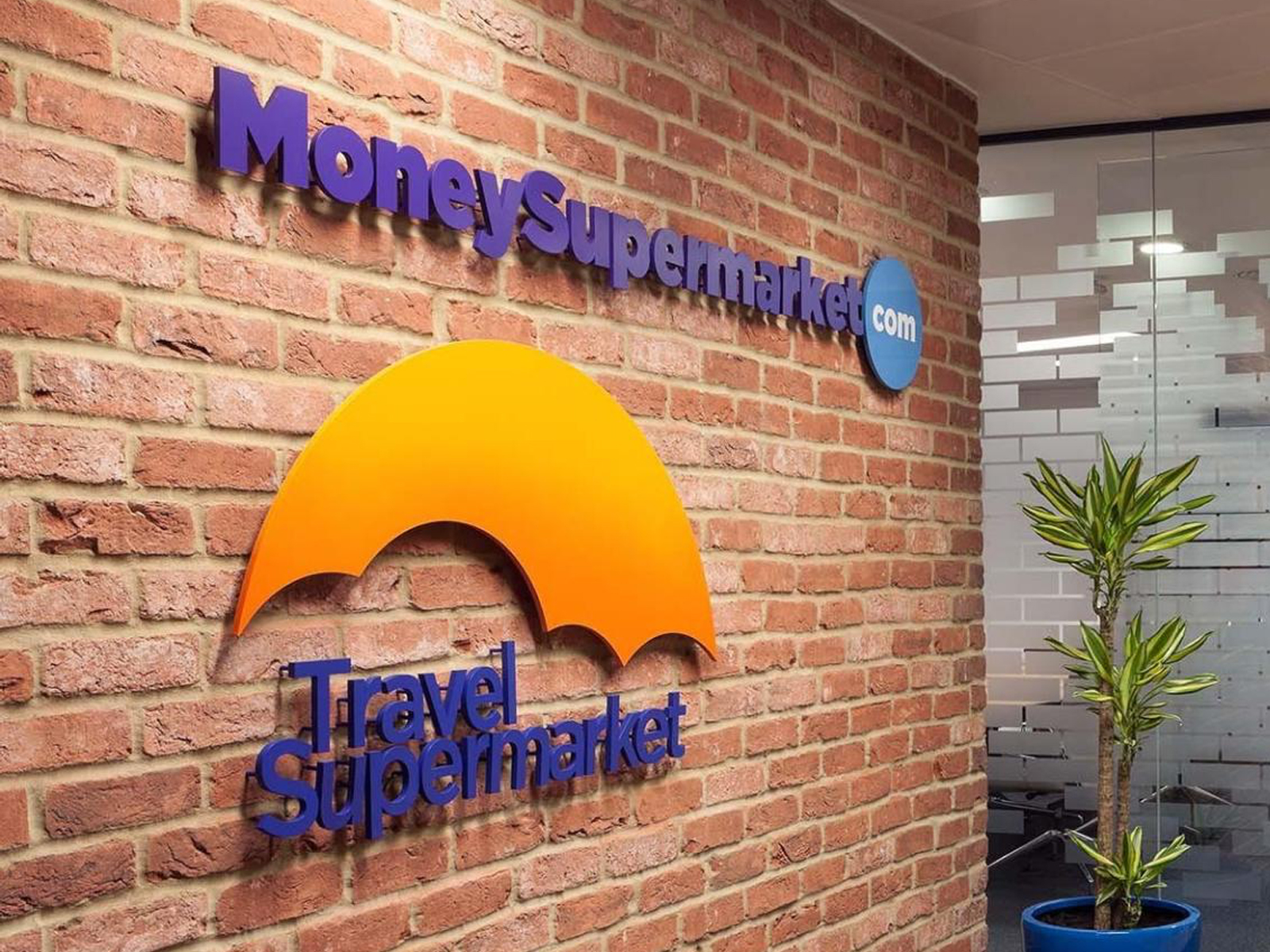 Photograph of Moneysupermarket office interior showing their logo on an exposed brick wall